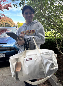Person holding a white bag with a brand logo, standing outdoors.
