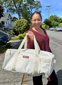 Woman holding a white duffel bag with a visible brand logo on a street.
