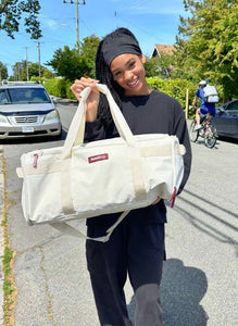 Person holding a white tote bag with a brand logo on a street.
