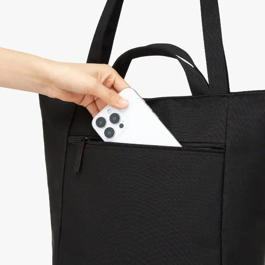 Hand placing a smartphone into a black tote bag.
