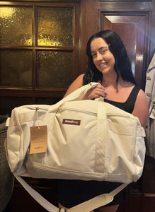 Woman holding a beige duffel bag with a visible brand tag indoors.