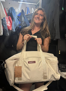 Woman holding a beige bag with a visible brand logo in a clothing store setting