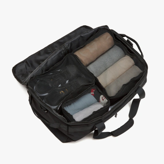 Black travel bag with compartments containing folded clothes on a white background