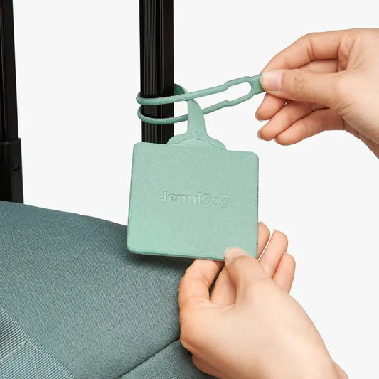 Person attaching a green luggage tag to a suitcase.