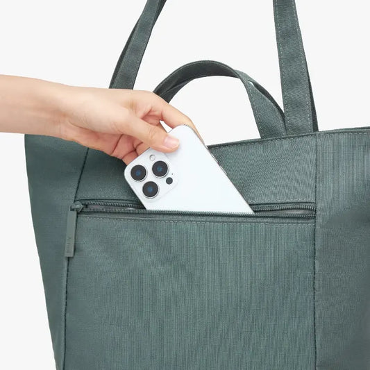 Person placing a white smartphone into a green tote bag.