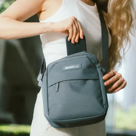 Person holding a gray JenniBag with a phone on a blurred background.