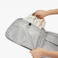 Person placing a shoe into a gray shoe bag on a white background