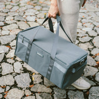 Person carrying a gray duffel bag on a cobblestone street.