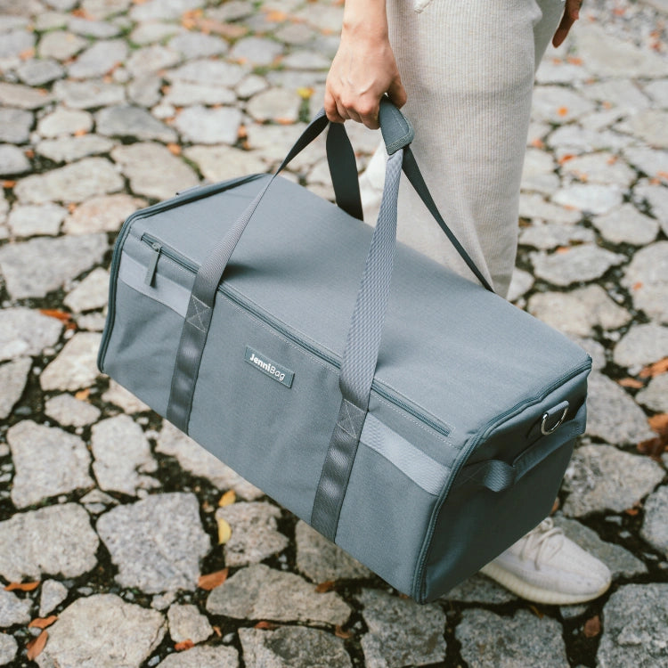 Person carrying a gray duffel bag on a cobblestone street.