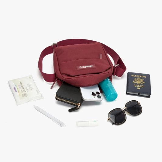 Red crossbody bag with travel items including a phone, passport, and sunglasses on a white background.