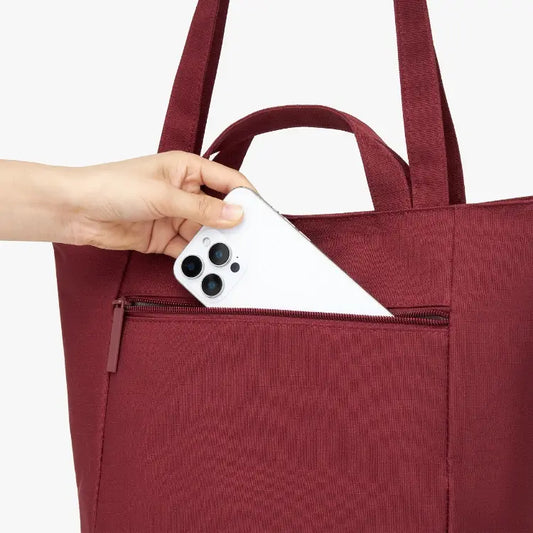 Person placing a white phone into a maroon tote bag.