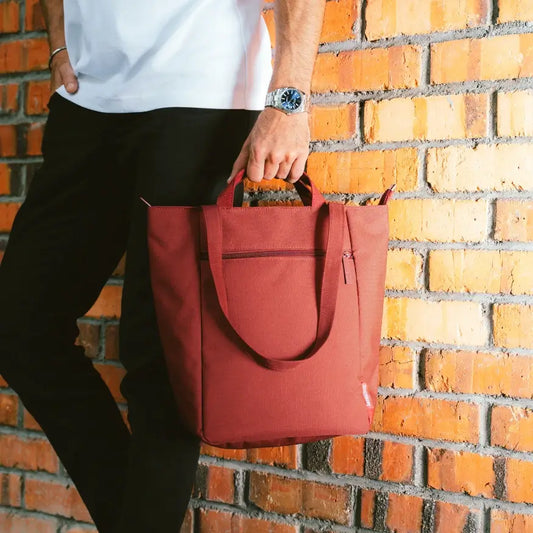 Person holding a red tote bag against a brick wall