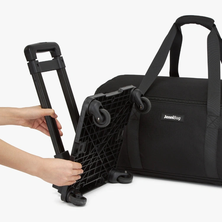 Black rolling suitcase being adjusted with a person's hand on a white background.