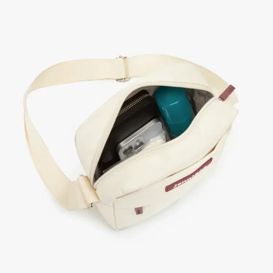 Beige crossbody bag with contents on a white background