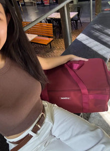 Person holding a red suitcase in an outdoor setting