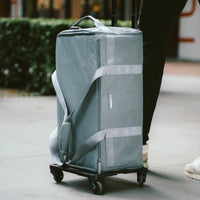 Gray rolling suitcase being pushed on a sidewalk.