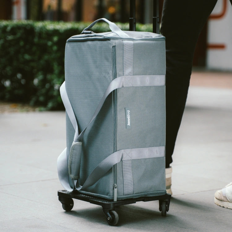 Gray rolling suitcase being pushed on a sidewalk.