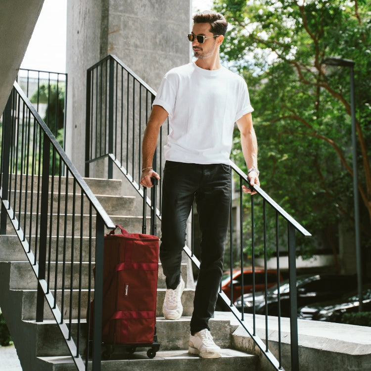 Man walking down stairs with a red bag, wearing a white t-shirt and dark pants.
