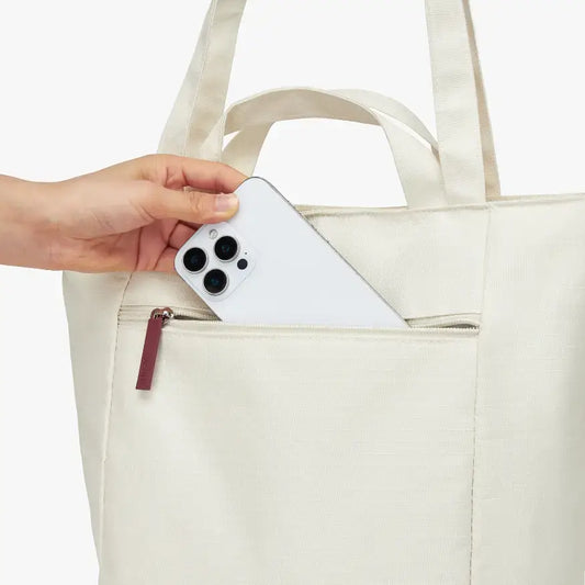 Person placing a smartphone into a beige tote bag on a white background