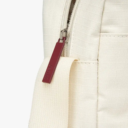 Close-up of a red zipper pull on a beige fabric background.