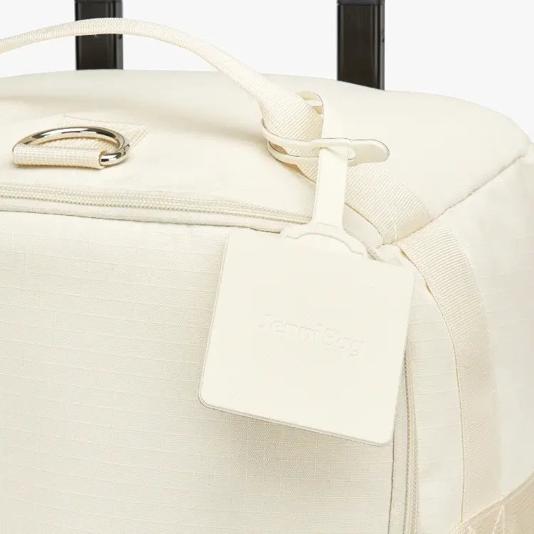 Close-up of a cream suitcase with a luggage tag.