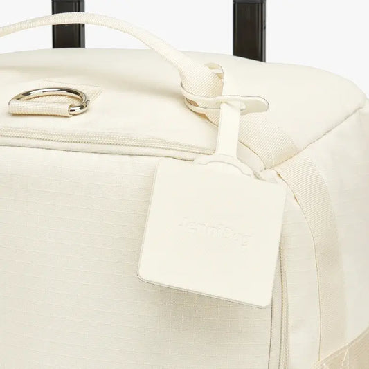 Close-up of a cream suitcase with a luggage tag.
