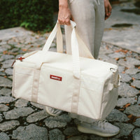 Person holding a beige duffel bag on a cobblestone path.