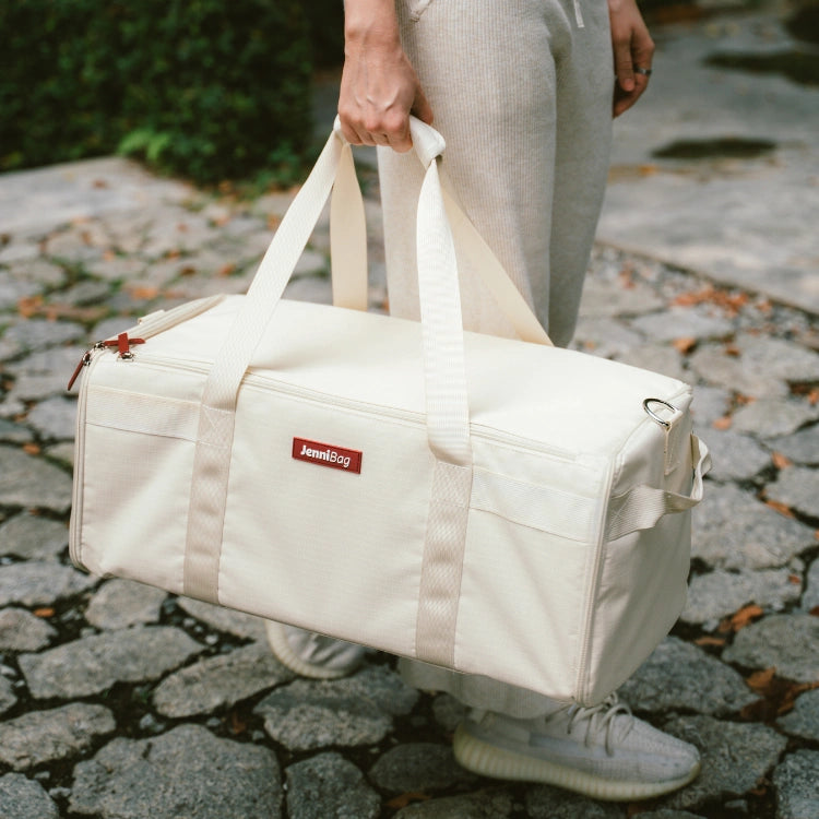 Person holding a beige duffel bag on a cobblestone path.