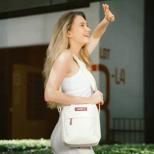 Woman in white top with a white bag, arms raised in excitement.