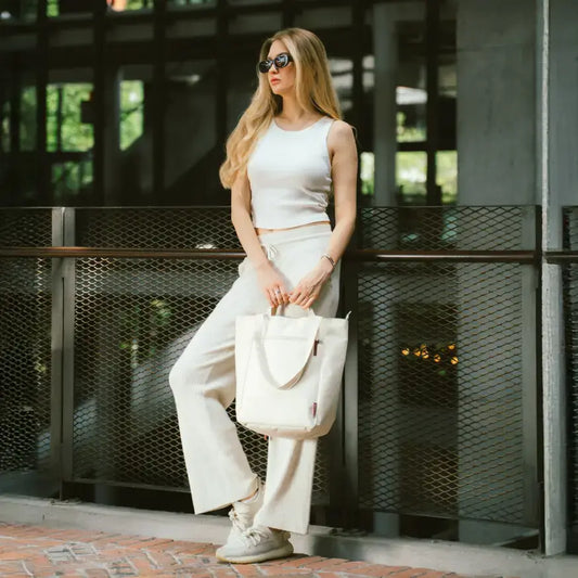 Woman in white outfit holding a white bag outdoors