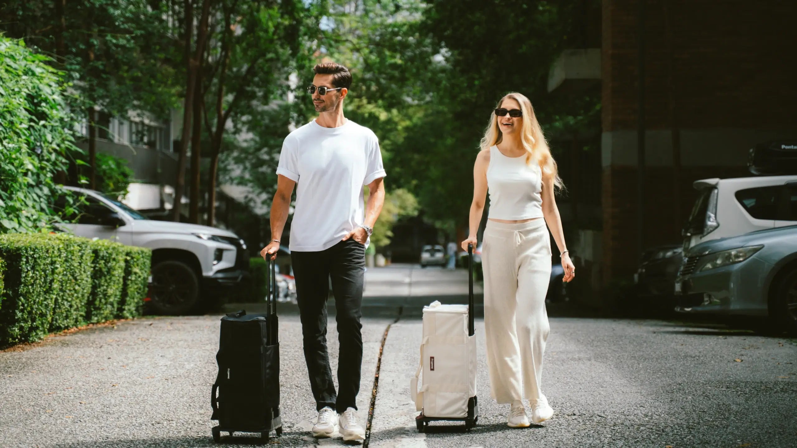 Two people walking with suitcases on a street.