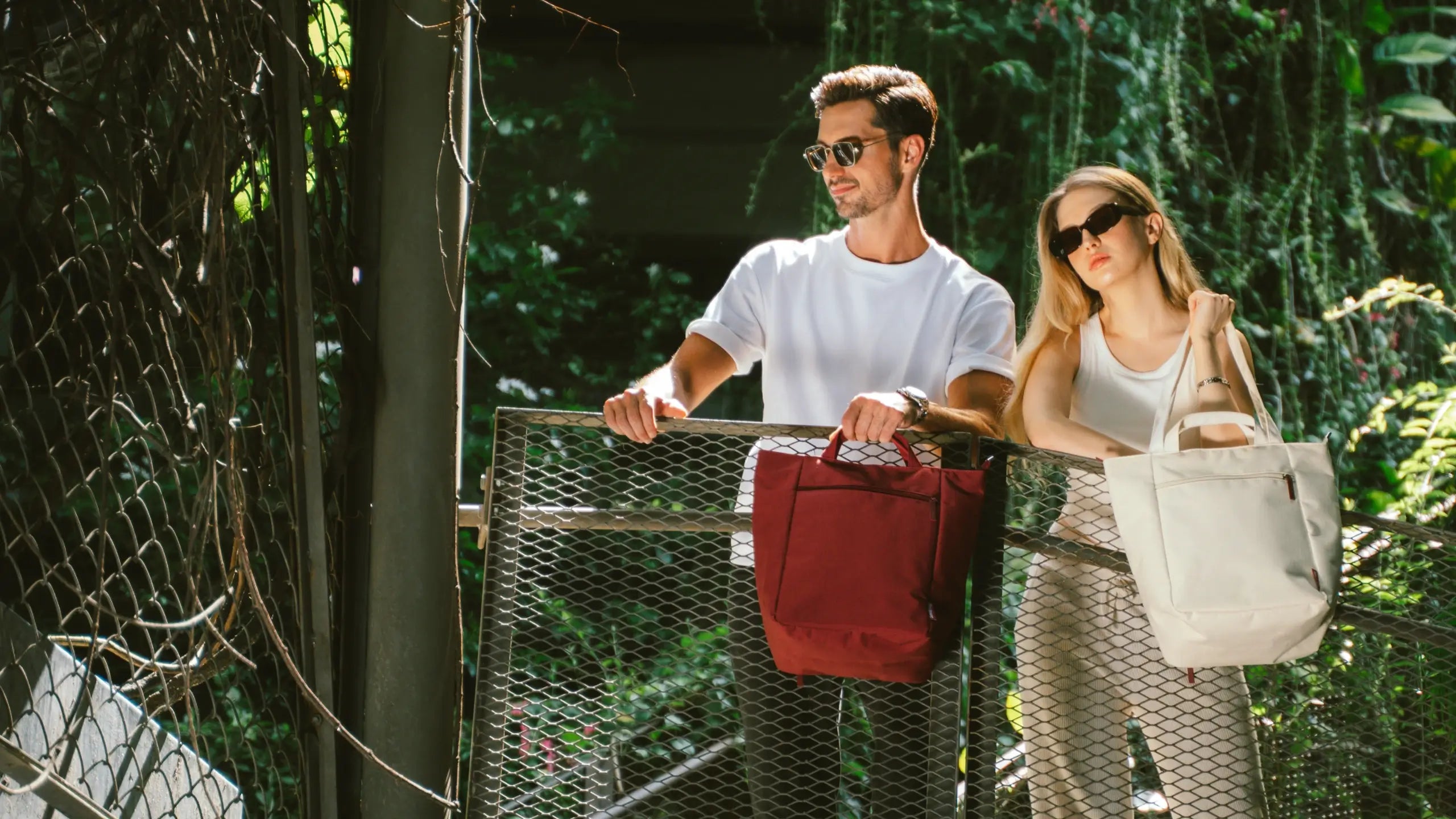 Two people holding bags on a bridge with greenery in the background