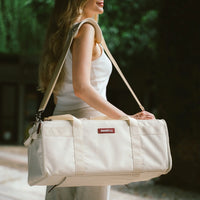 Woman carrying a beige tote bag with a strap outdoors.