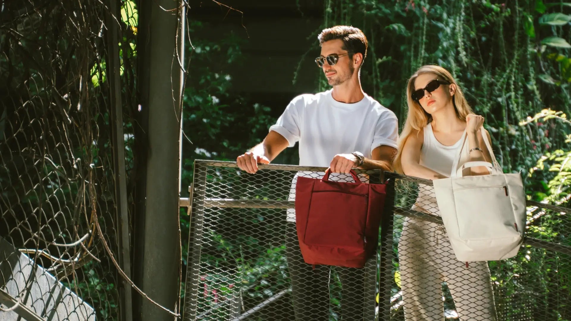 Two people with shopping bags and a red bag in a forested area.