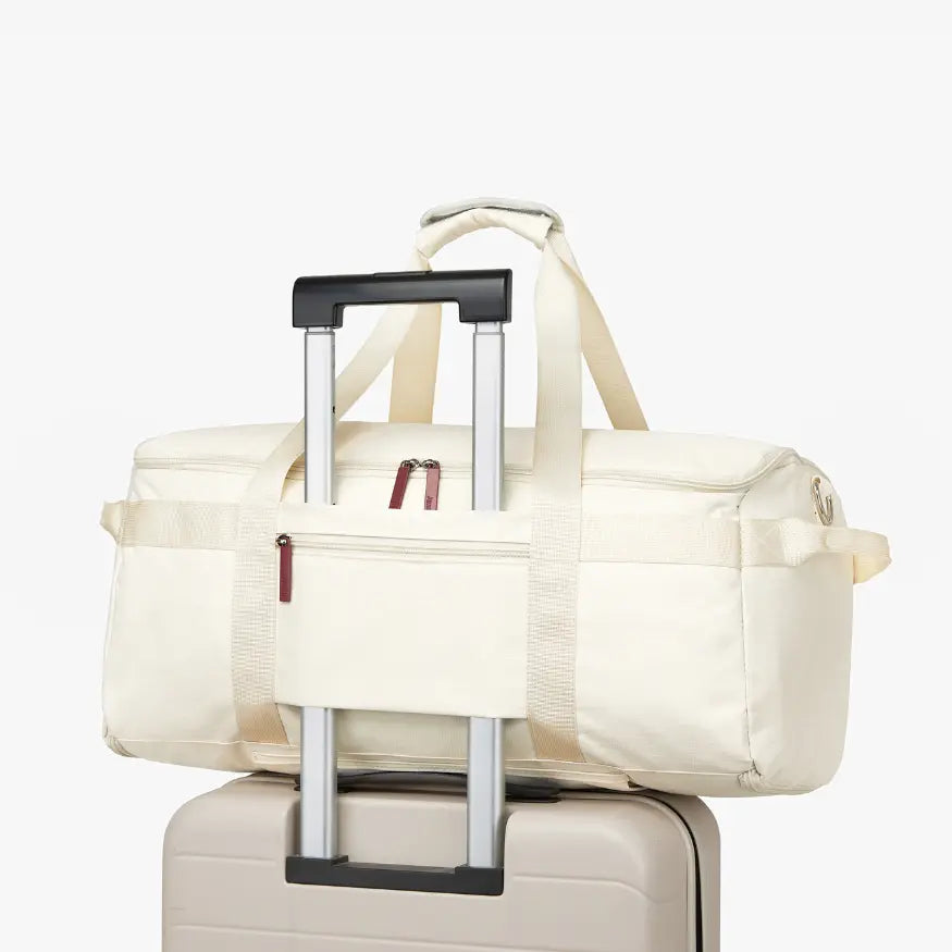 White duffel bag with wheels attached to a suitcase on a white background