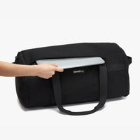 Black duffel bag with a laptop being placed inside on a white background