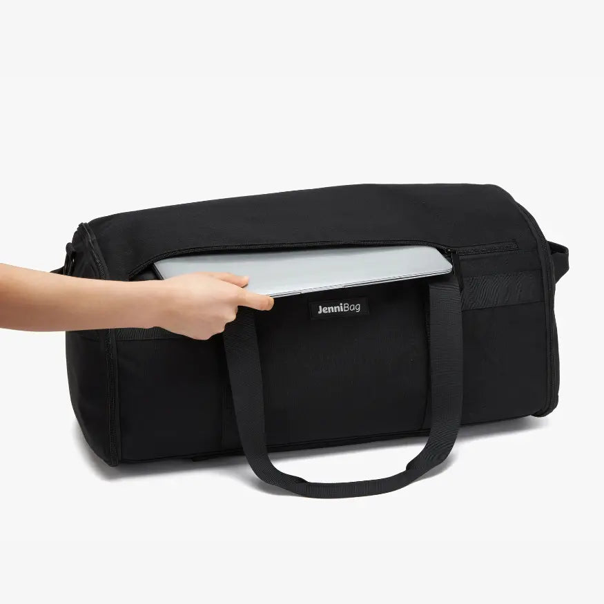Black duffel bag with a laptop being placed inside on a white background