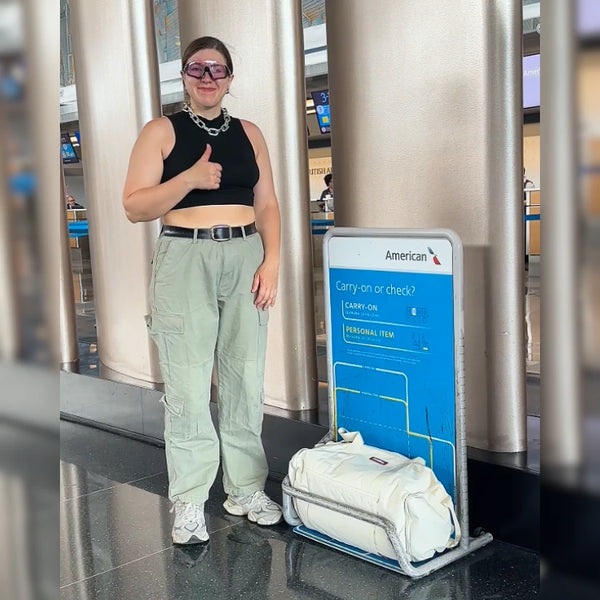 Traveler giving a thumbs-up beside American Airlines’ carry-on sizer with a cream JenniBag in it
