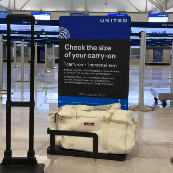 Cream JenniBag at the base of a United Airlines carry-on sizer in front of a “Check the size of your carry-on” sign