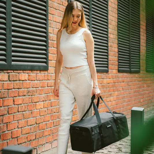 Woman holding a black duffel bag against a brick wall.