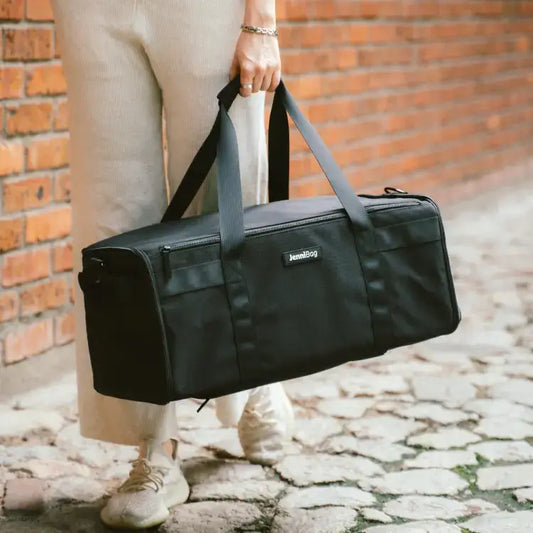 Person holding a black duffel bag against a brick wall background