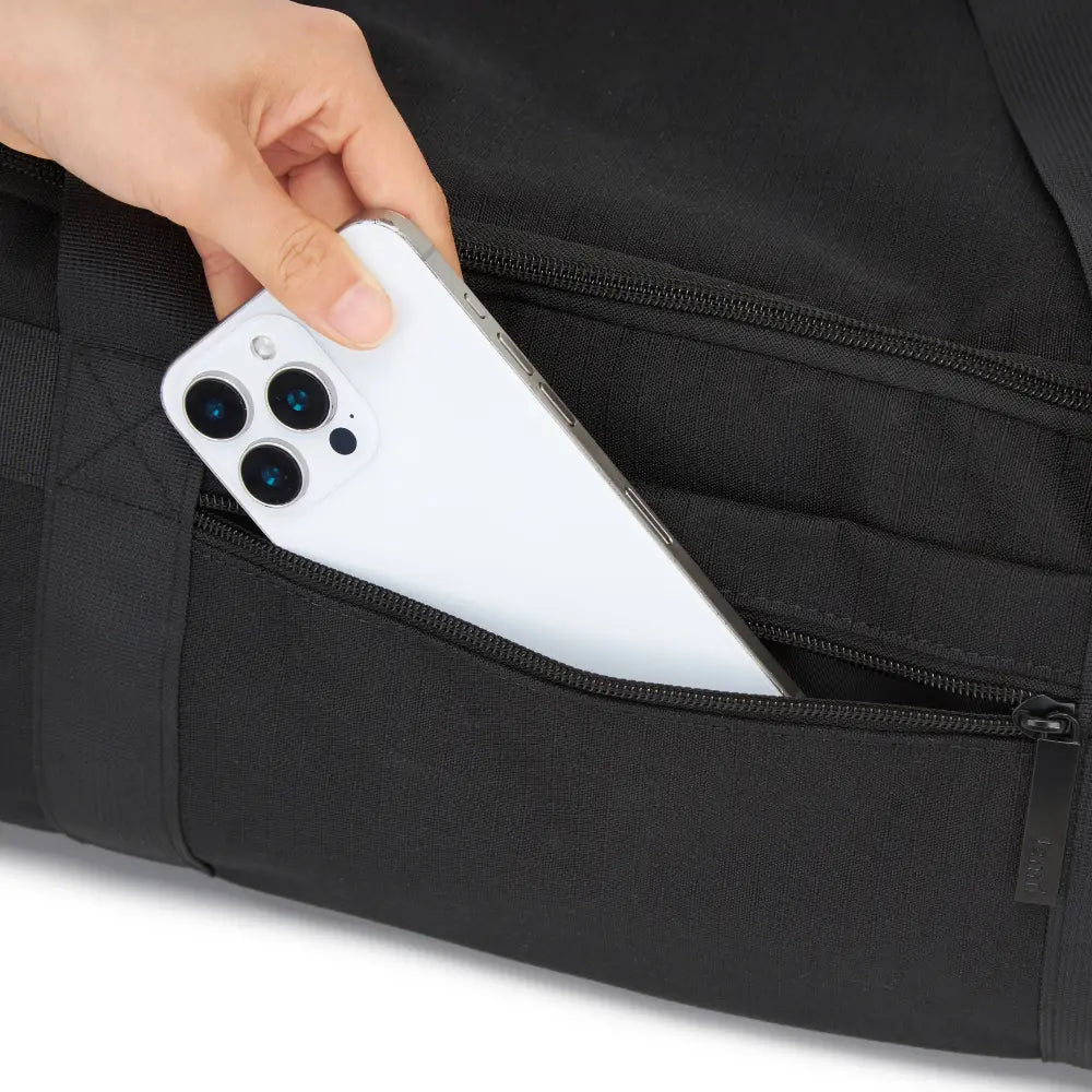 A phone being slipped into an external zip pocket on the black bag.